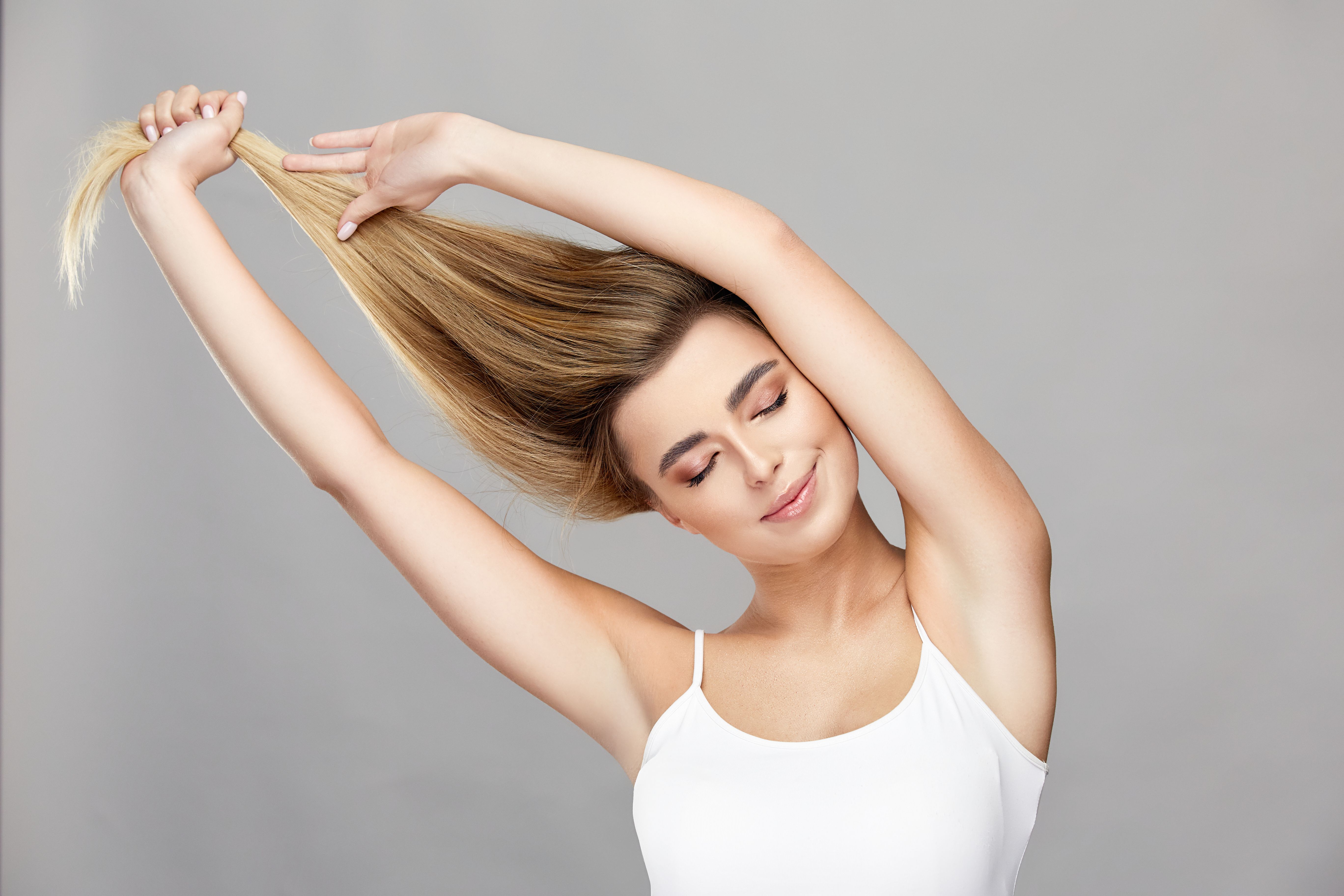 beautiful woman with natural make-up and perfect smile pulling up her healthy blond hair wearing white shirt, cute girl with super long blondy hair